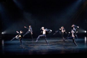 Five dancers moving across a stage.
