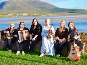 Six musicians holding their instruments and poising outside in front of water and mountains
