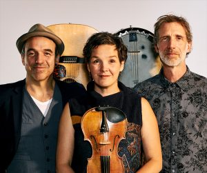 Three musicians with two guitars in the background and violin in the forefront